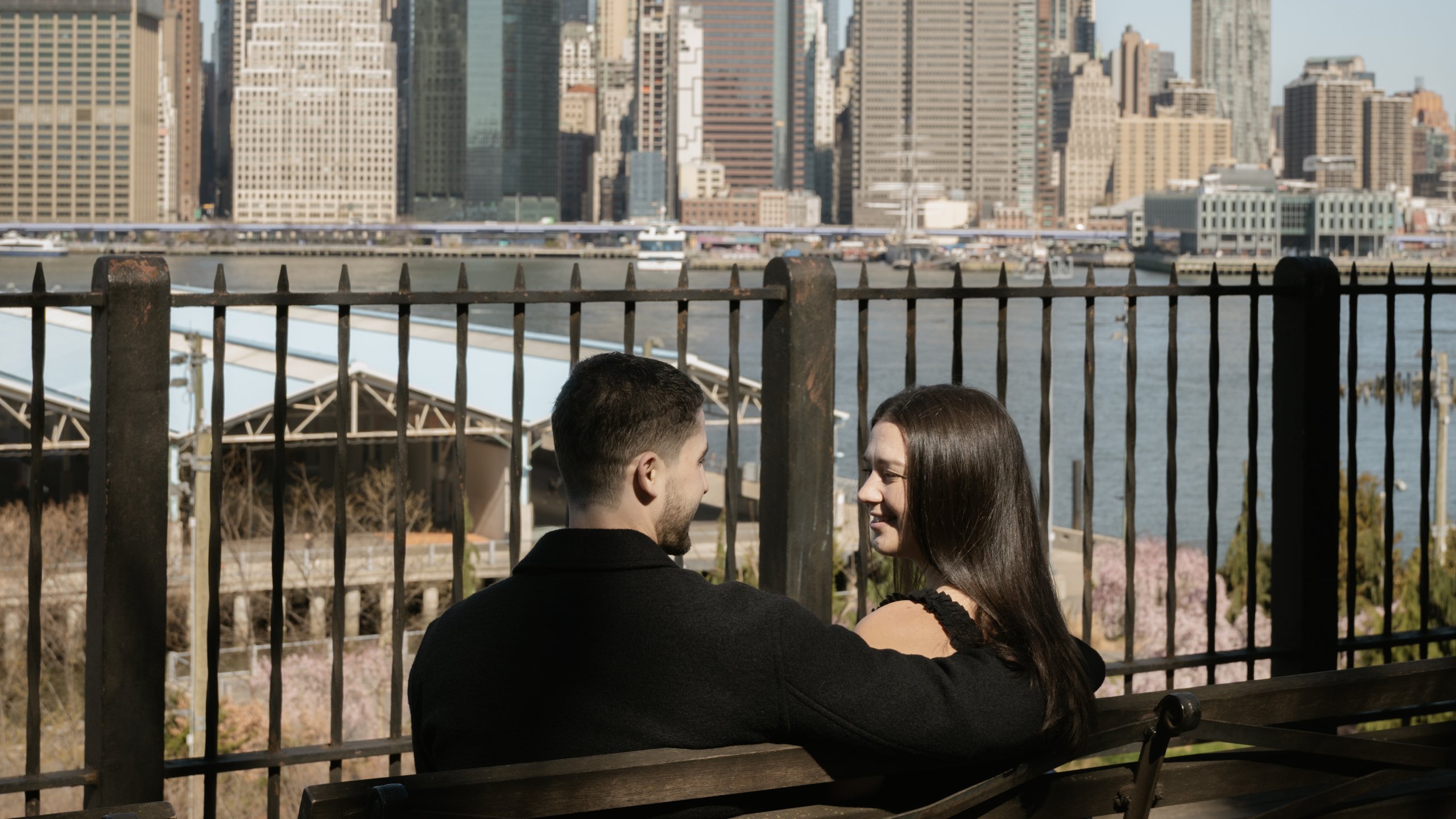 Taylor and Jake on a bench at the Brooklyn Heights Promenade with the Manhattan skyline behind them